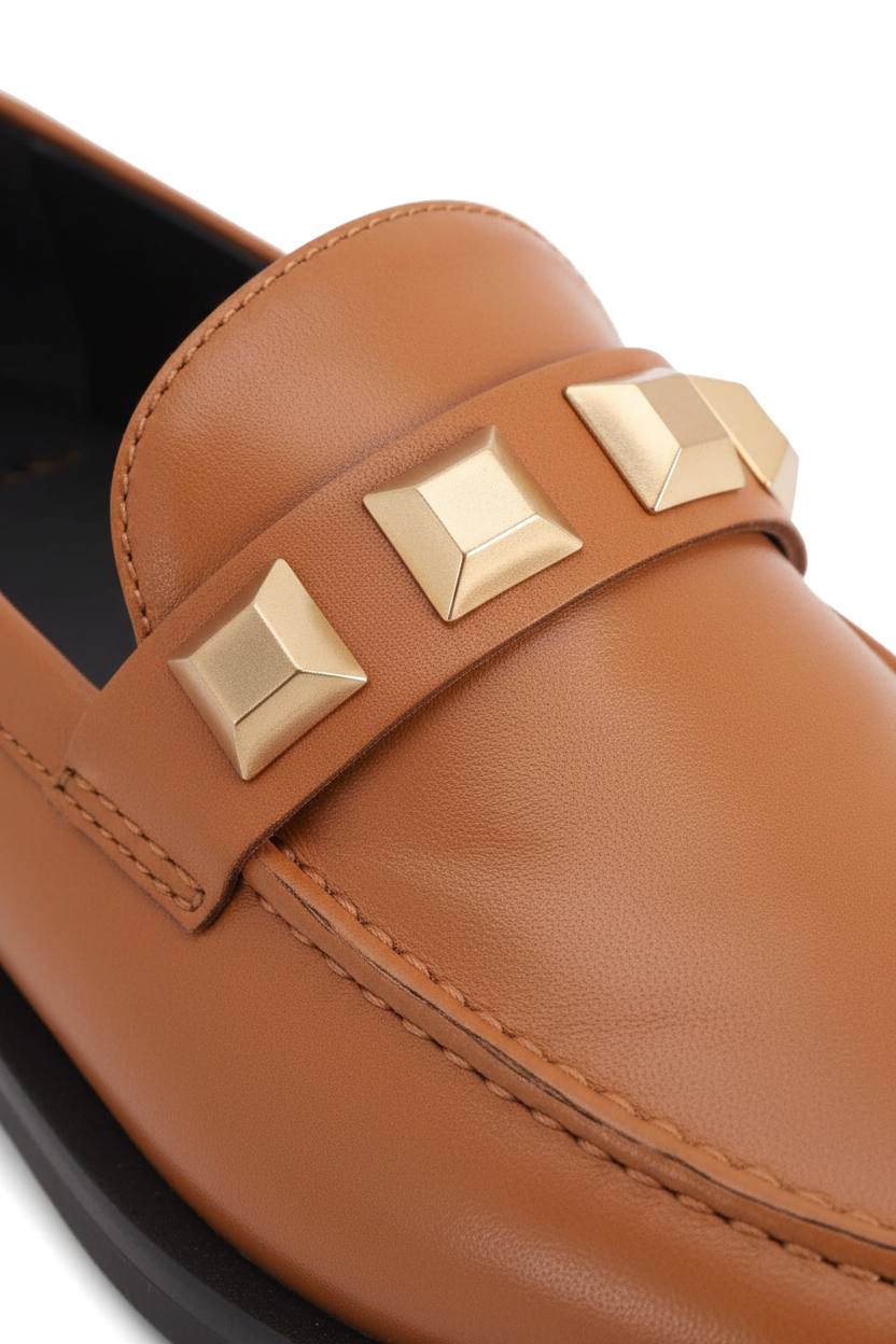 Close up detail of the alternating diamond and pyramid gold studs on the Caete caramel loafers