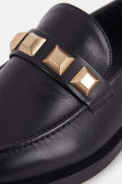 Close up detail of the three gold pyramid studs on the vamp strap of the Caete black loafers