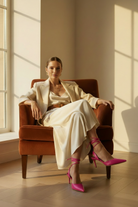 Woman wearing Mangará Jaborandi pink leather slingback pointed-toe heels, seated lifestyle editorial photo