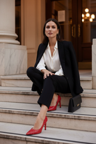 Callisia red studded leather pumps styled with black tailored trousers and an ivory silk shirt on pale marble theatre steps at dusk