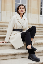 Andira black leather shearling ankle boots styled with an ivory belted cocoon wool coat and slim black trousers on pale stone steps in winter